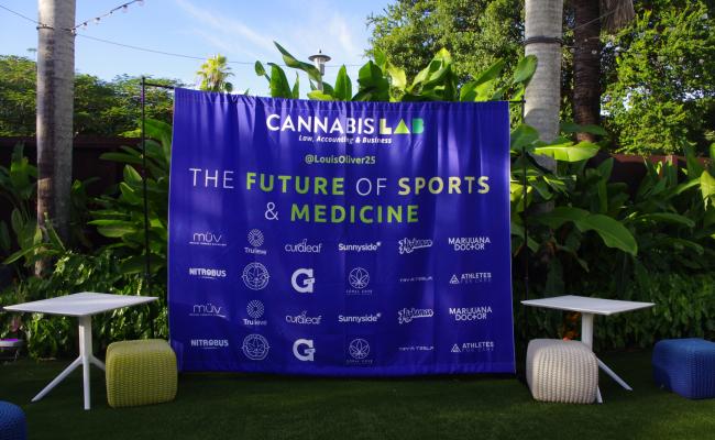 The future of sports & medicine event in Miami, Florida with Marijuana Doctor MMJ doctors picturing a blue promotional sign with medical cannabis brands listed & tropical plants in the background 