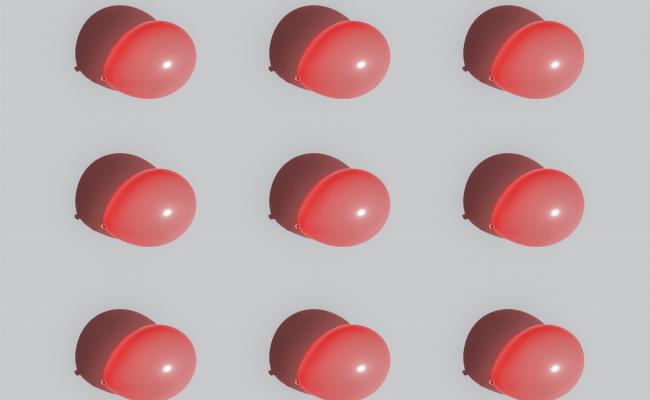 Nine red blown up balloons aligned in rows of three against a white background
