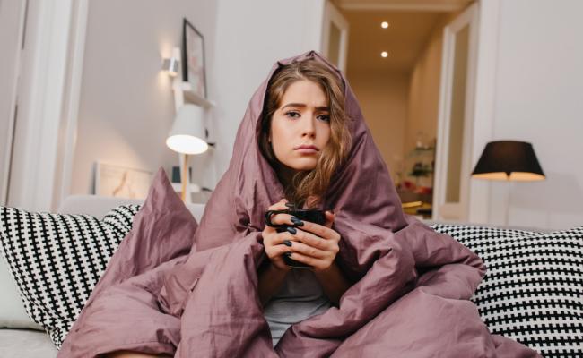 Womanon sofa, wrapped in a blanket with a warm cup in her hand