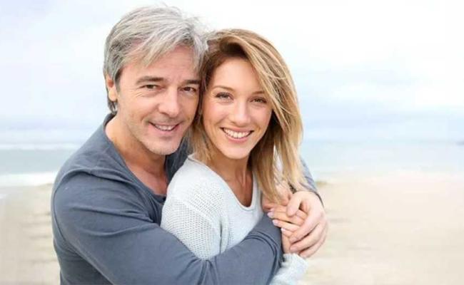 A mature couple on the beach smiling into the camera