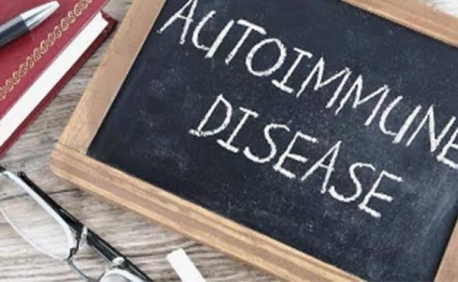 Notebook with a pen laying on it and glasses on the surface beside a small chalkboard with "Autoimmune Disease" written in chalk upon it.