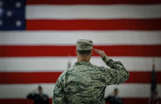 A uniformed Veteran saluting the American Flag.