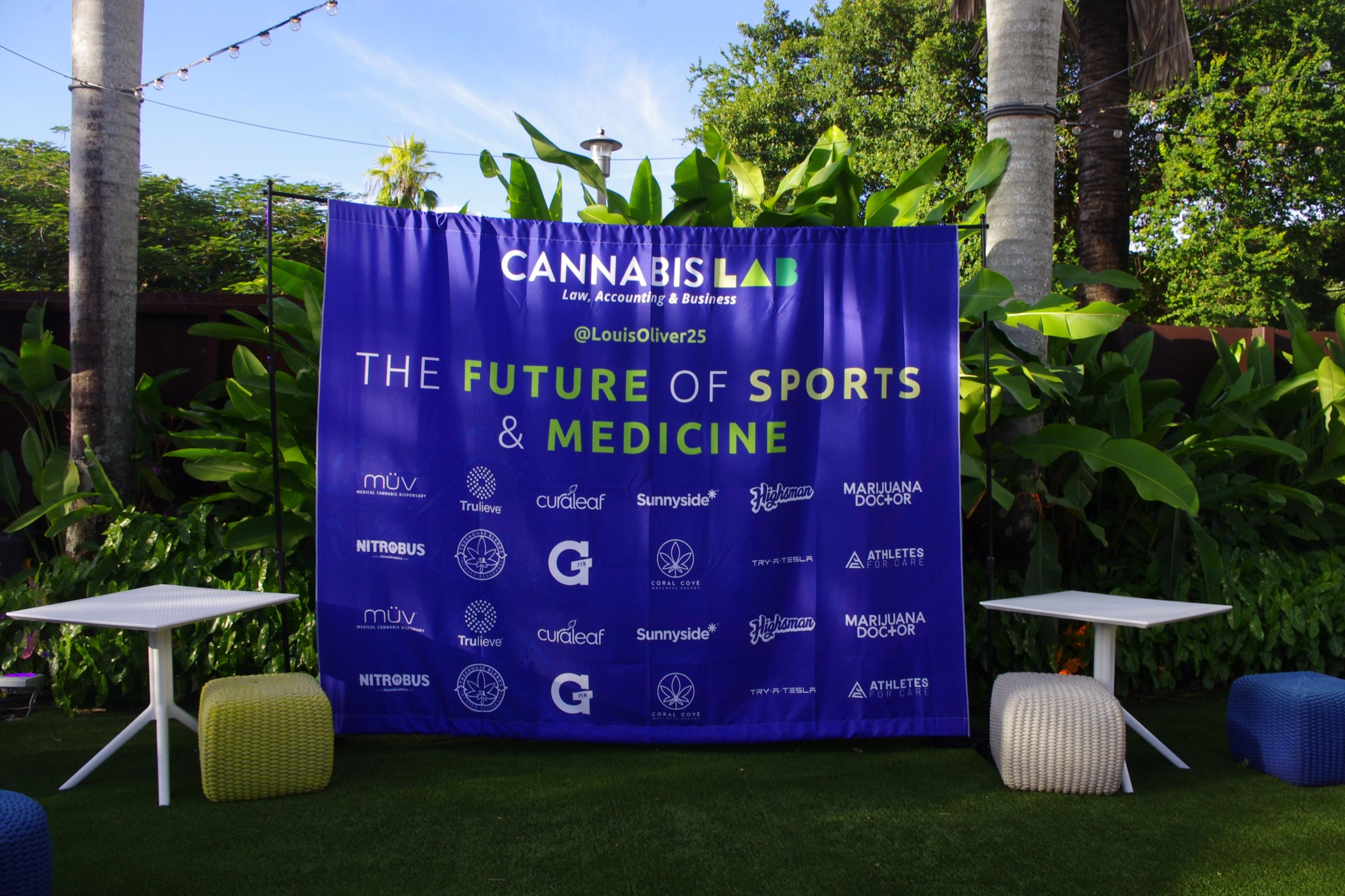 The future of sports & medicine event in Miami, Florida with Marijuana Doctor MMJ doctors picturing a blue promotional sign with medical cannabis brands listed & tropical plants in the background 