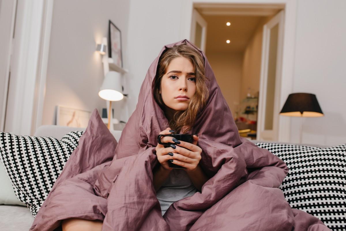 Womanon sofa, wrapped in a blanket with a warm cup in her hand