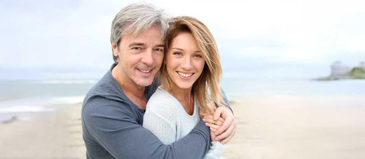 A mature couple on the beach smiling into the camera