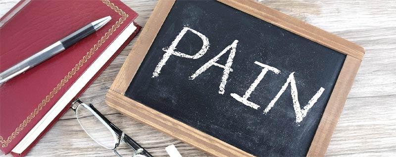 A chaalkboard laying flat on a table with the  word "PAIN" wrriten on it.